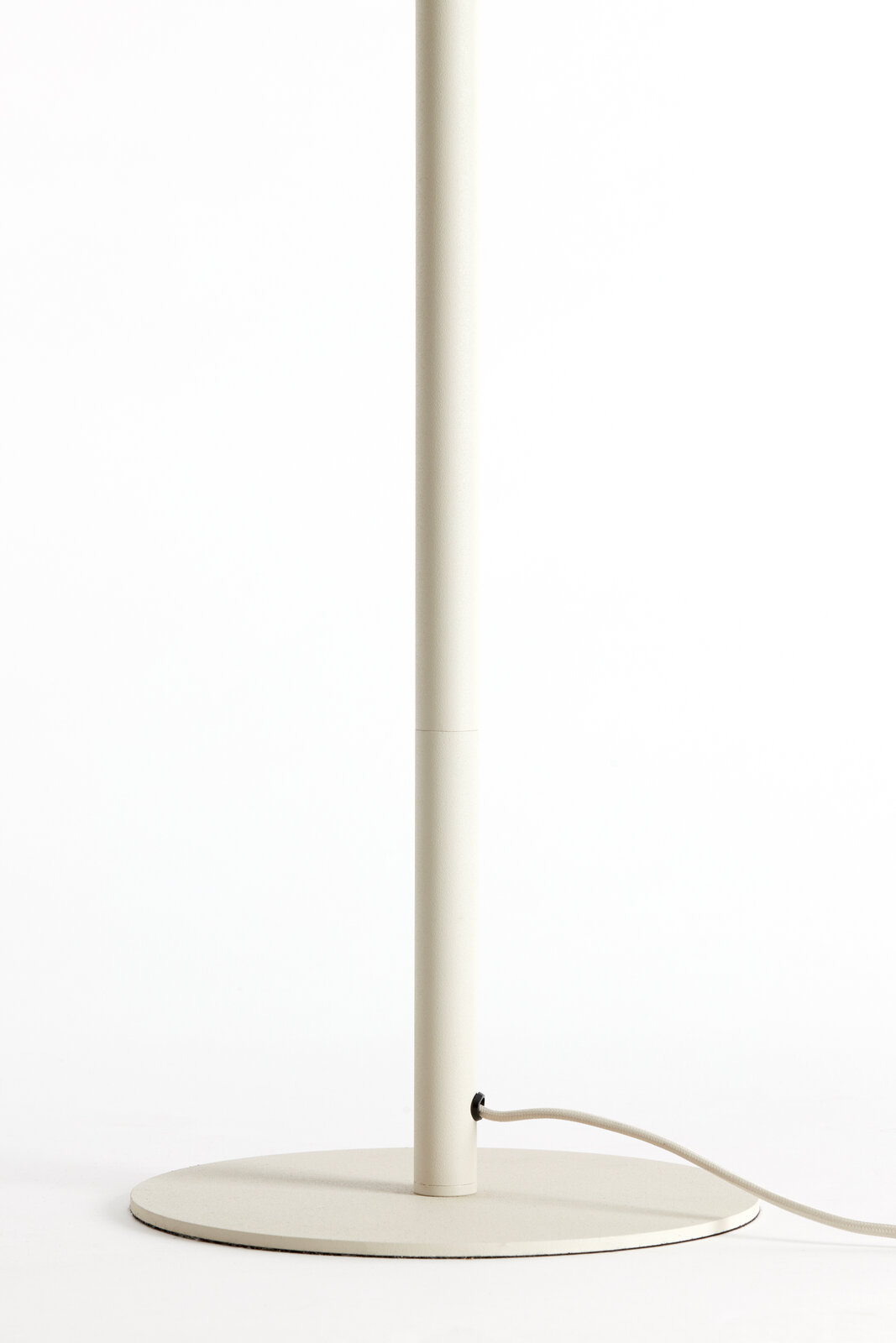 Nahaufnahme des unteren Teils einer Stehleuchte mit rundem Sockel und Stromkabel, seitliche Perspektive.