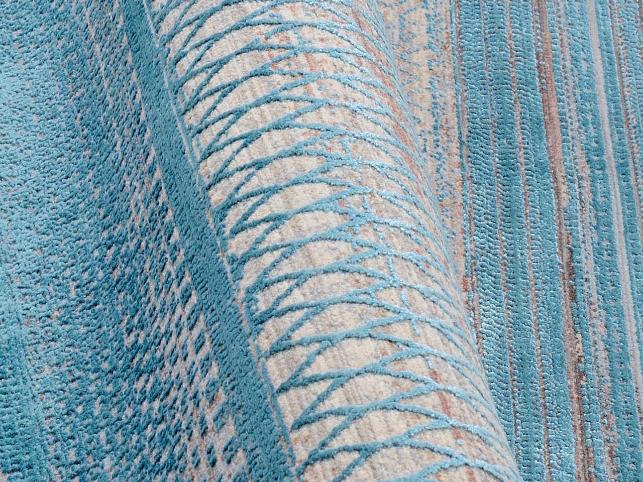 Nahaufnahme eines Designer-Teppichs mit blauem und beigem geometrischem Muster, teilweise aufgerollt.
