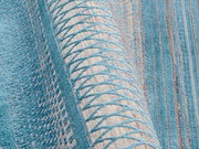 Nahaufnahme eines Designer-Teppichs mit blauem und beigem geometrischem Muster, teilweise aufgerollt.