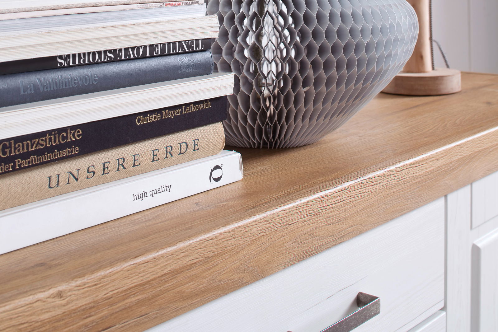 Nahaufnahme eines Sideboards mit Holzoberfläche, darauf Bücher und eine dekorative Vase, Perspektive von schräg oben.