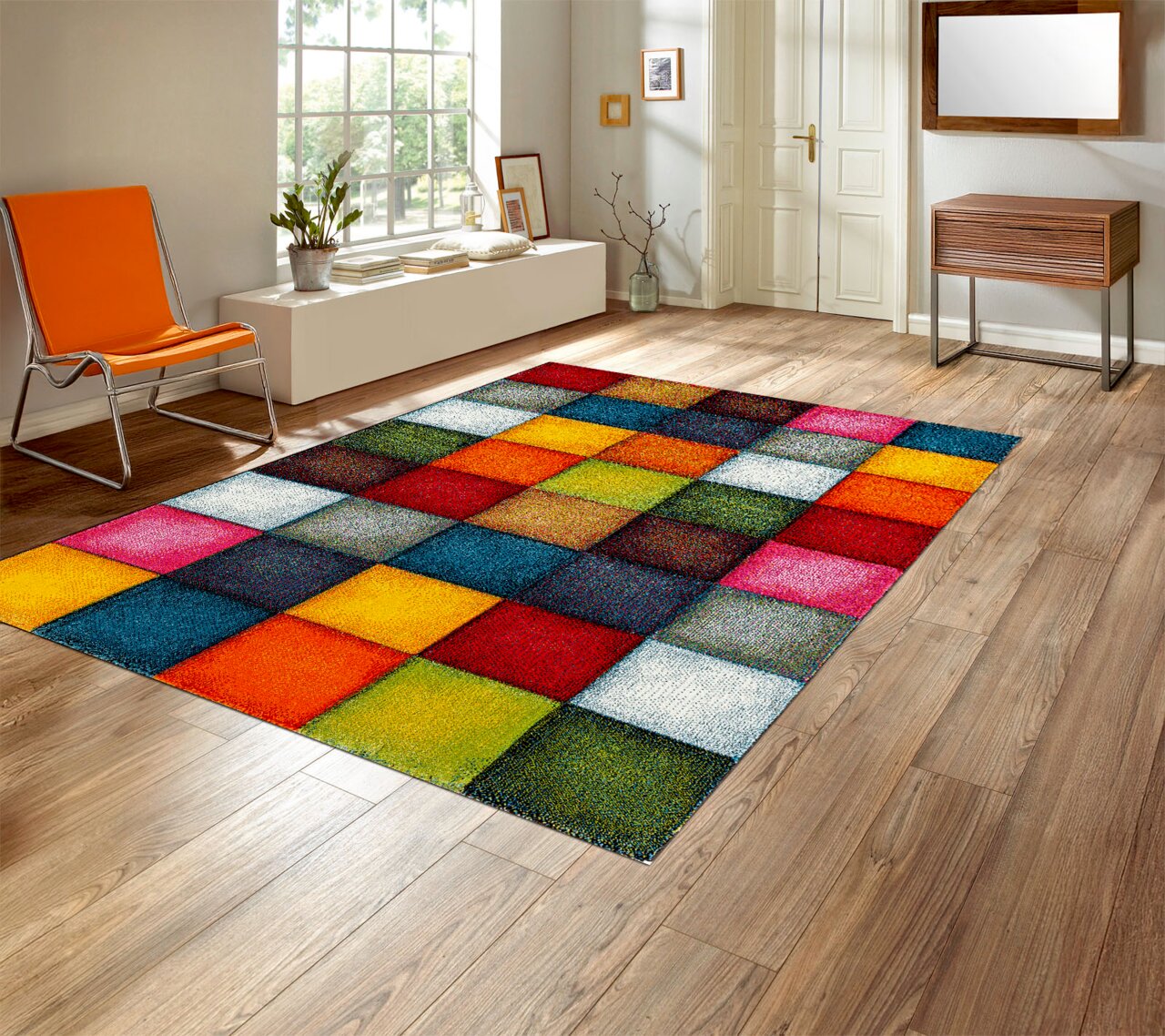 Bunter Patchwork-Teppich mit quadratischem Muster in kräftigen Farben (Rot, Blau, Gelb, Grün, Pink) in einem hellen Wohnzimmer auf Holzfußboden, perspektivische Ansicht schräg von oben