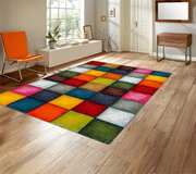 Kleurrijk patchwork-tapijt met vierkant patroon in felle kleuren (rood, blauw, geel, groen, roze) in een lichte woonkamer met houten vloer, perspectivisch aanzicht schuin van bovenaf