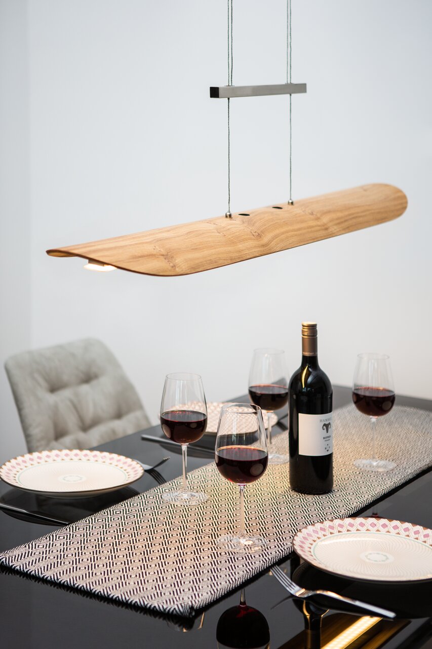 Zurbrüggen LED-Pendelleuchte COLOMBIA Moderne LED-Pendelleuchte aus Holz über einem gedeckten Esstisch mit Weinflaschen und Gläsern, seitliche Perspektive.