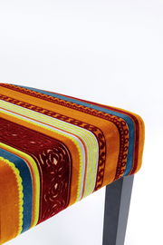 Nahaufnahme eines Stuhlsitzes mit buntem, gestreiftem Stoffbezug in warmen Farben, von oben betrachtet.