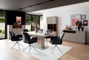 Modernes Esszimmer mit hellem Esstisch und vier grauen Polster-Drehstühlen auf Teppich, dazu Sideboards und Vitrine in Beige-Holz-Optik; Perspektive: frontale, leicht erhöhte Weitwinkelansicht.