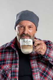 Mann mit grauer Mütze und kariertem Hemd hält eine Tasse mit der Aufschrift 'Thinking outside the box' in der Hand, frontal aufgenommen.