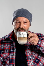 Mann mit grauer Mütze und kariertem Hemd hält eine Tasse mit der Aufschrift 'Thinking outside the box' in der Hand, frontal aufgenommen.