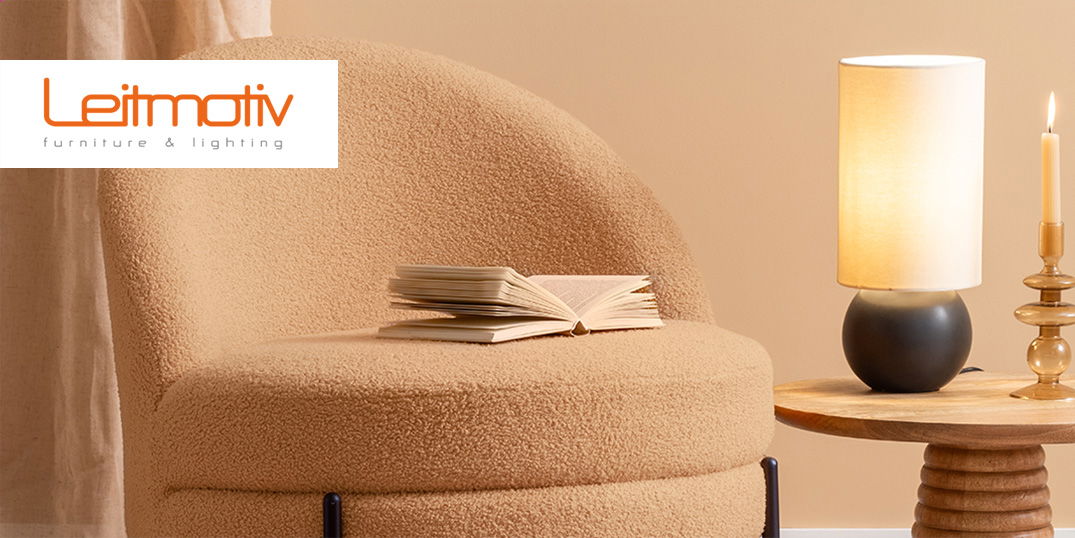 Beiger Sessel mit einem Buch neben einem Beistelltisch mit einer Lampe der Marke Leitmotiv.