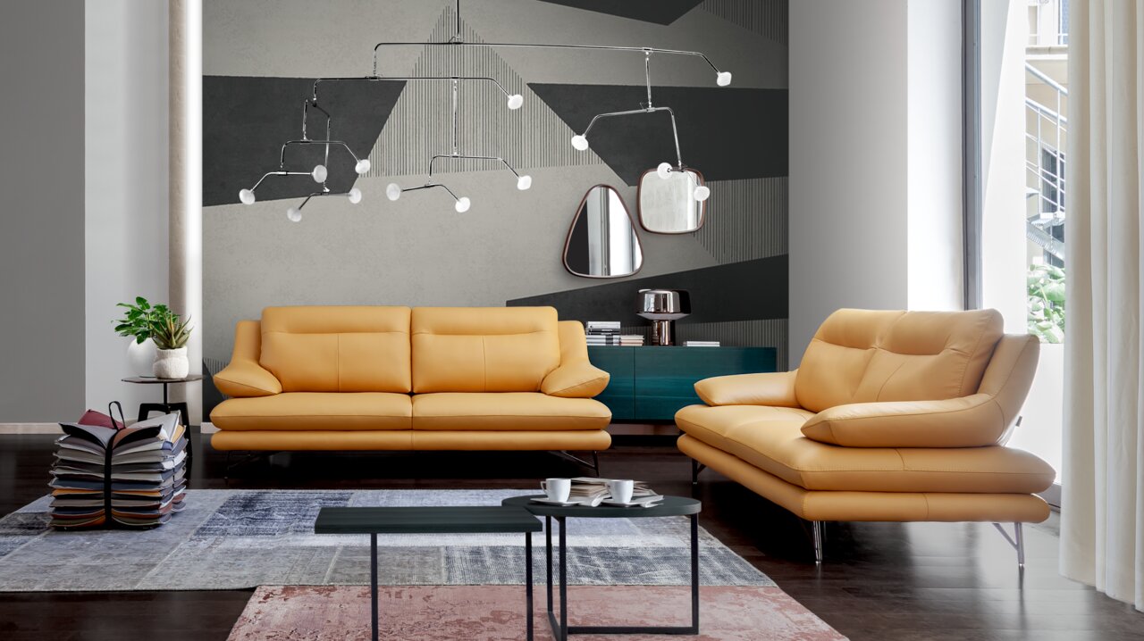 Modernes Wohnzimmer mit zwei gelben Sofas in Frontalansicht, dekoriert mit geometrischen Wandmustern und einem eleganten Kronleuchter.