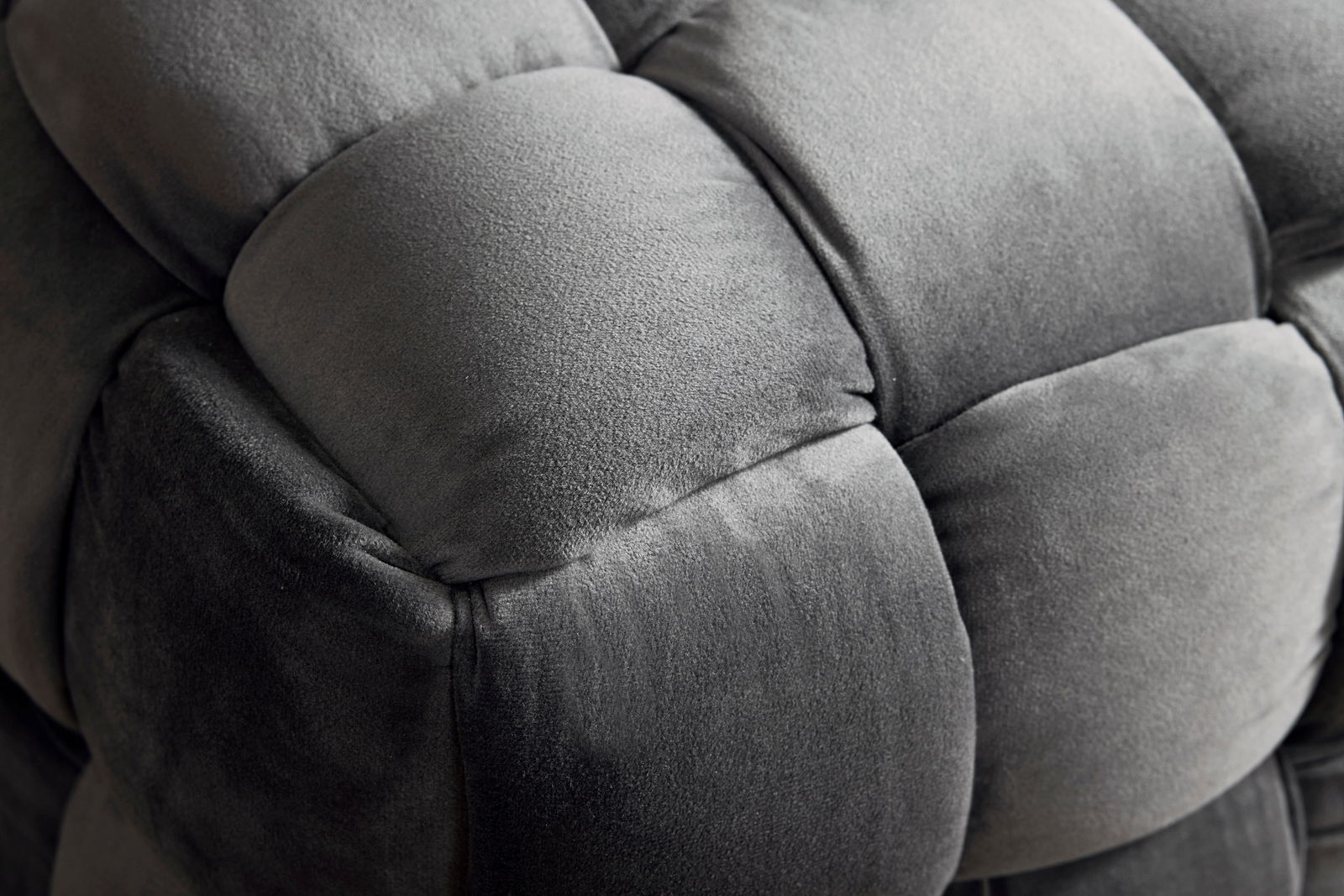 Nahaufnahme eines grauen, gepolsterten Hockers mit weicher, samtartiger Oberfläche.