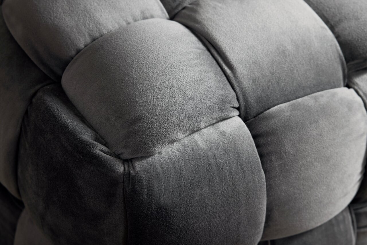 Nahaufnahme eines grauen, gepolsterten Hockers mit weicher, samtartiger Oberfläche.