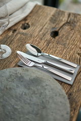 Nahaufnahme eines eleganten Bestecksets bestehend aus Messer, Gabel und Löffel auf einer grauen Serviette, auf einem rustikalen Holztisch arrangiert.