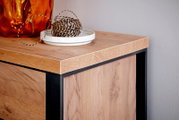 Nahaufnahme einer Ecke eines Eck-Schreibtisches aus Holz mit schwarzem Metallrahmen, dekoriert mit einer orangefarbenen Vase und einer Schale mit Schnur.