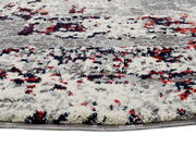 Nahaufnahme eines Designer-Teppichs mit abstraktem Muster in Grau, Rot und Blau. Perspektive von der Seite.
