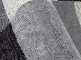 Nahaufnahme eines grauen Frisé-Teppichs mit geometrischem Muster, von der Seite betrachtet.