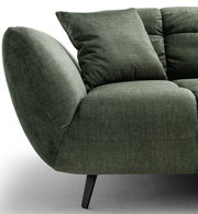 Detailansicht eines grünen Stoffsofas mit abgerundeter Armlehne, Sitzkissen und Rückenkissen auf schwarzen Metallfüßen, Perspektive schräg von vorne links