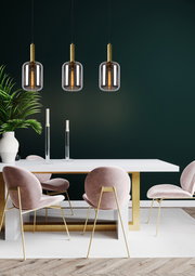 Drei moderne Pendelleuchten JOANET mit goldenen Akzenten hängen über einem eleganten Esstisch mit rosa Samtstühlen, seitliche Perspektive.