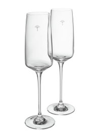 Zwei elegante Champagnergläser aus klarem Glas mit langem Stiel, von der Seite betrachtet, mit dezentem Logo auf dem Kelch.
