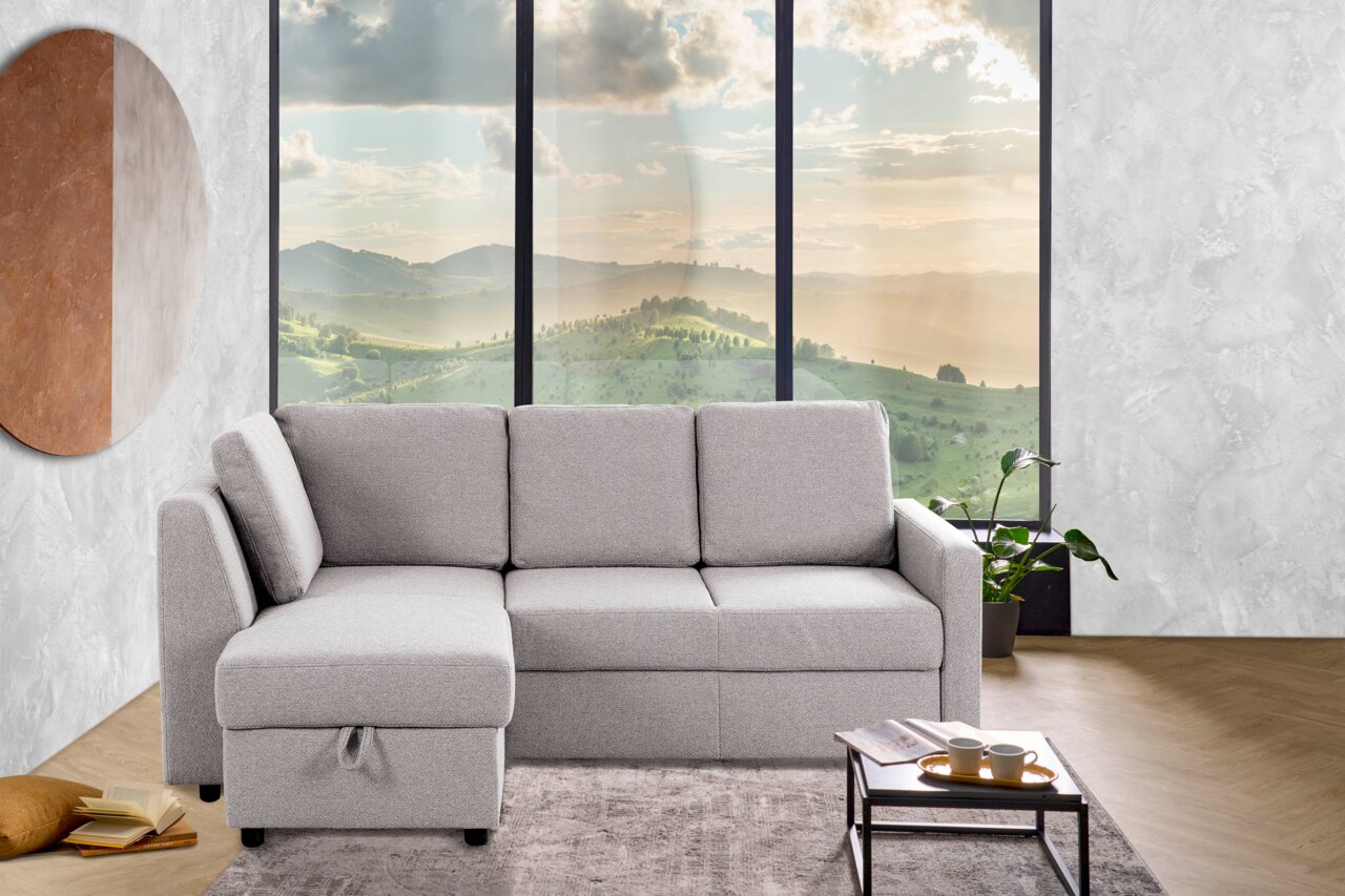 Graues Ecksofa mit Blick auf die linke Seite, vor einem großen Fenster mit Landschaftsausblick, auf einem Teppich stehend.