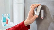Hand befestigt einen tesa Powerstrip Waterproof Haken an einer Badezimmerwand, seitliche Perspektive.