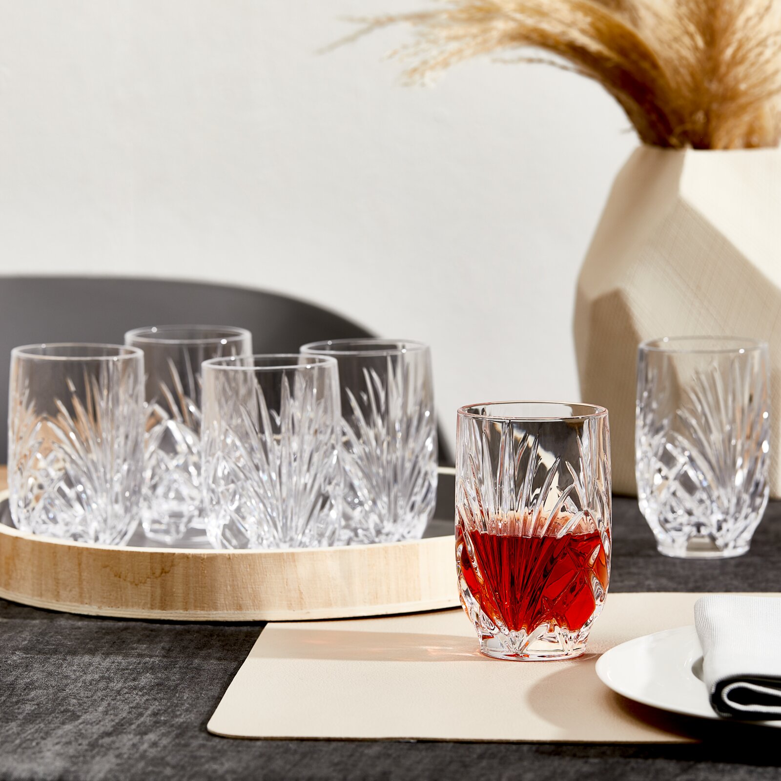 Kristallglas-Set mit elegantem Schliff in frontaler Perspektive auf einem gedeckten Tisch, ein Glas im Vordergrund mit rotem Getränk gefüllt
