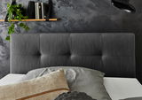 Boxspringbett mit grauem Kopfteil, dekoriert mit Kissen, im modernen Schlafzimmer mit dunkler Wand und Regal im Hintergrund, seitliche Perspektive