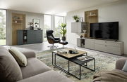 Modernes Wohnzimmer mit einem eleganten Sideboard in dunklem Grau, umgeben von stilvollen Möbeln und Dekorationen. Perspektive von der Seite.