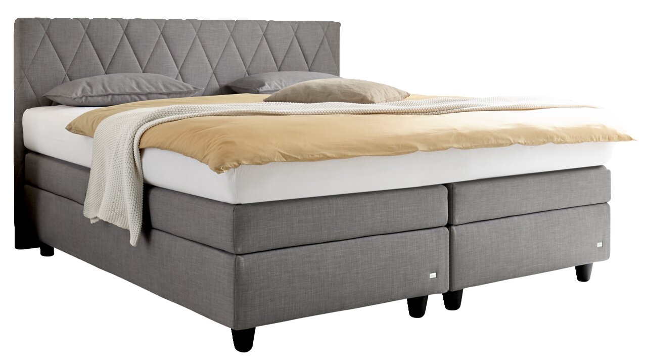 Graues Boxspringbett mit gestepptem Kopfteil, seitliche Perspektive