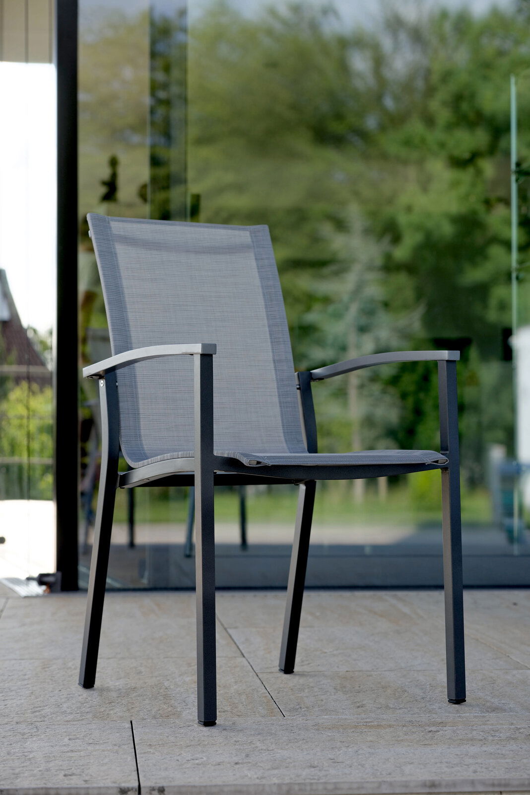 Moderner Stapelsessel aus Metall mit grauem Textilgewebe, seitliche Perspektive auf einer Terrasse.