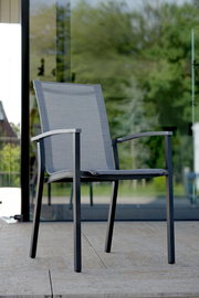 Moderner Stapelsessel aus Metall mit grauem Textilgewebe, seitliche Perspektive auf einer Terrasse.