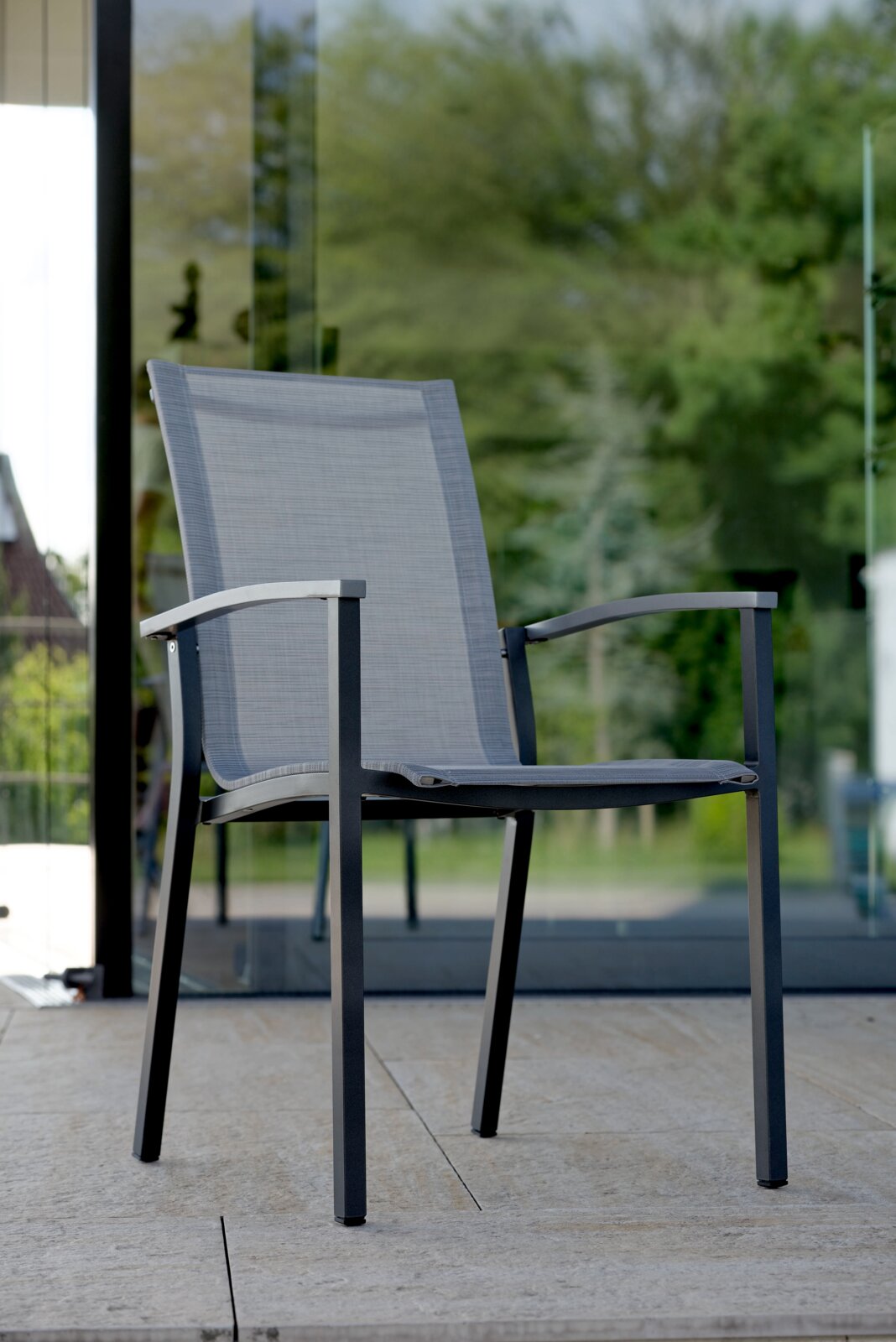 Moderner Stapelsessel aus Metall mit grauem Textilgewebe, seitliche Perspektive auf einer Terrasse.