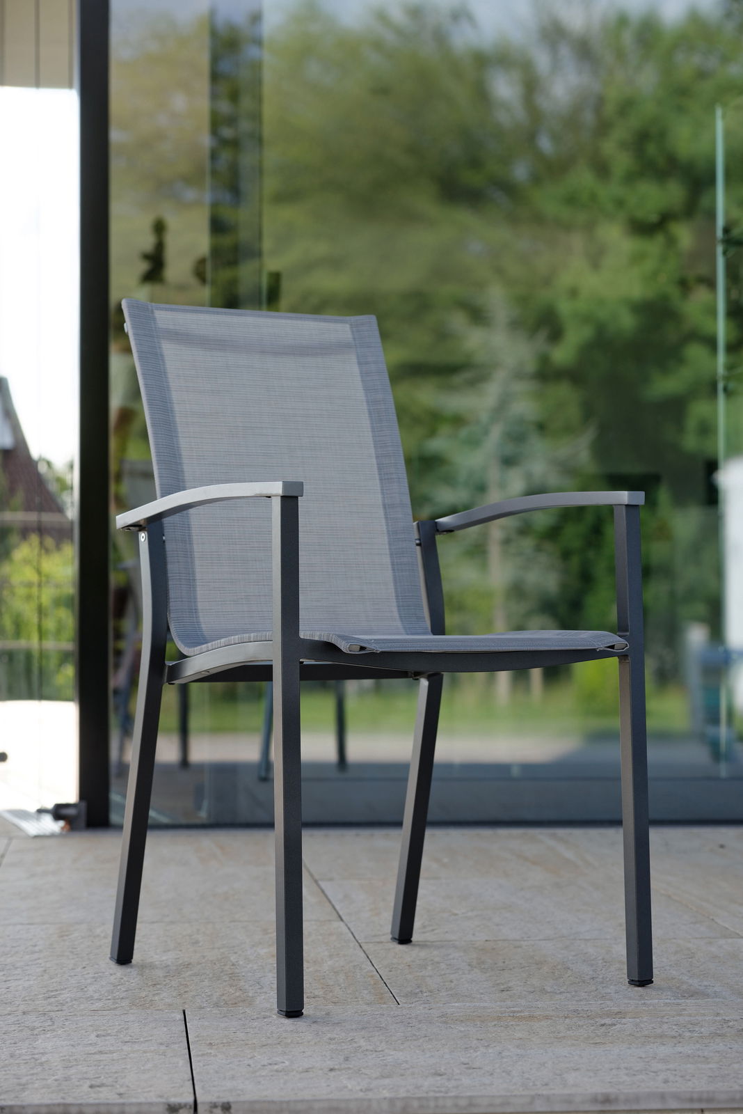 Moderner Stapelsessel aus Metall mit grauem Textilgewebe, seitliche Perspektive auf einer Terrasse.
