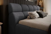Seitliche Perspektive auf ein elegantes Polsterbettgestell mit dunkelgrauem Kopfteil und bequemen Kissen.