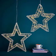 Zwei hängende LED-Sterne mit warmweißen Lichtern vor einer blauen Wand, seitliche Perspektive.