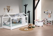 Een rolcontainer op wieltjes in een kinderkamer, gevuld met speelgoed, naast een wit huisbed en planken. Perspectief: zijaanzicht.