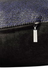 Nahaufnahme einer Zierkissenhülle mit feinem, strukturiertem Stoff in dunklen Tönen und einem silbernen Reißverschlussanhänger mit der Aufschrift 'JOOP!'.