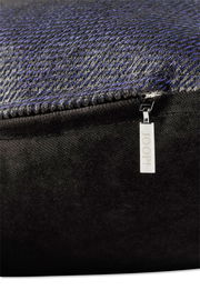 Nahaufnahme einer Zierkissenhülle mit feinem, strukturiertem Stoff in dunklen Tönen und einem silbernen Reißverschlussanhänger mit der Aufschrift 'JOOP!'.