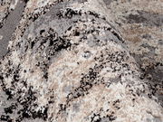 Nahaufnahme eines strukturierten Teppichs in Beige-, Grau- und Schwarztönen, perspektivisch von der Seite aufgenommen.