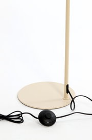 Detailaanzicht van de beige ronde lampvoet met slanke staander, zwart snoer en zwarte voetschakelaar, schuin van voren gefotografeerd