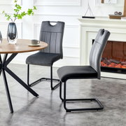 Zwei moderne Freischwinger-Esszimmerstühle in Dunkelgrau mit gepolsterter Sitzfläche und Rückenlehne, schwarzem Metallgestell und Ziernähten, seitliche Perspektive im Wohn-/Essbereich neben rundem Holztisch und Kamin.