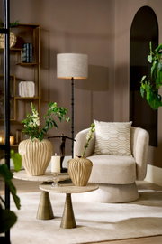 Sfeervolle moderne woonkamer vanuit vooraanzicht met crèmekleurige fauteuil, ronde bijzettafels, geribbelde vazen, vloerlamp en organische wandspiegel.