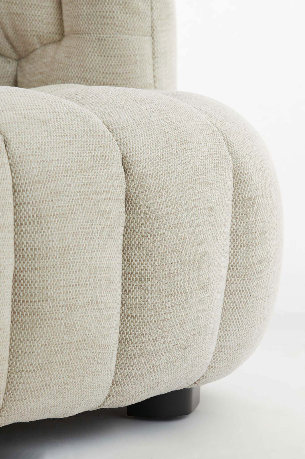 Nahaufnahme einer beigen Couch mit strukturierter Polsterung und abgerundeten Formen, seitliche Perspektive