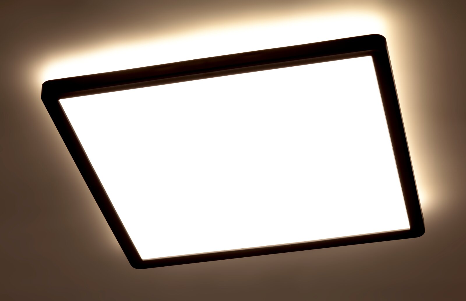 Quadratische LED-Deckenleuchte mit schwarzem Rahmen, von unten betrachtet, leuchtet hell an der Decke.