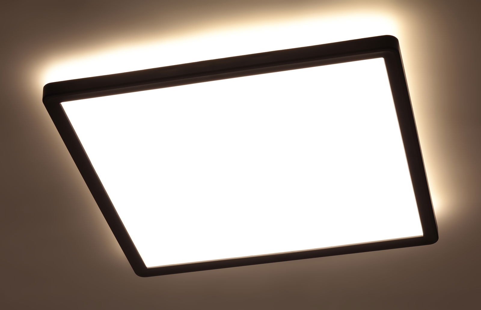 Quadratische LED-Deckenleuchte mit schwarzem Rahmen, von unten betrachtet, leuchtet hell an der Decke.