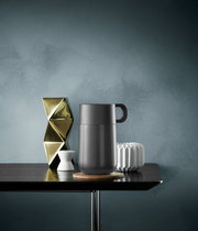 Impulse Travel Mug 0,3l Cromar in seitlicher Perspektive auf einem Tisch, umgeben von dekorativen Objekten.