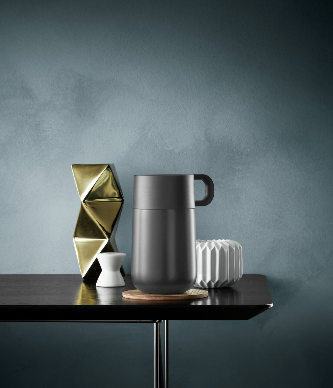 Impulse Travel Mug 0,3 l Cromar in zijaanzicht op een tafel, omringd door decoratieve voorwerpen.