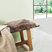 Lammfell Sitzauflage auf einer Holzbank, seitliche Perspektive, mit Blick auf ein Fenster mit Gartenblick.