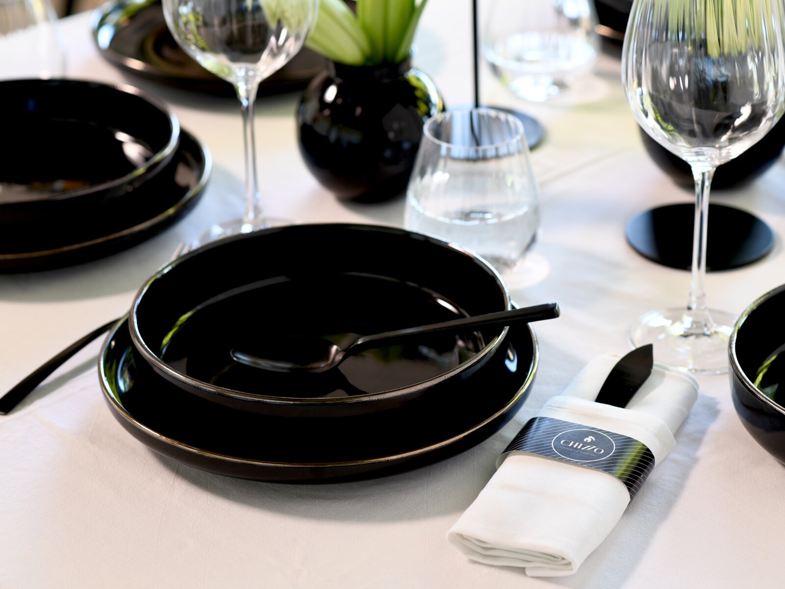 Elegant gedeckter Tisch mit schwarzem Geschirr, Besteck und Weingläsern auf weißer Tischdecke, schräg von oben aus der Nahperspektive fotografiert