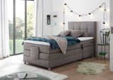 Graues Boxspringbett in einem modernen Schlafzimmer, seitliche Perspektive, mit dekorativen Kissen und Decke, umgeben von stilvollen Lichterketten.