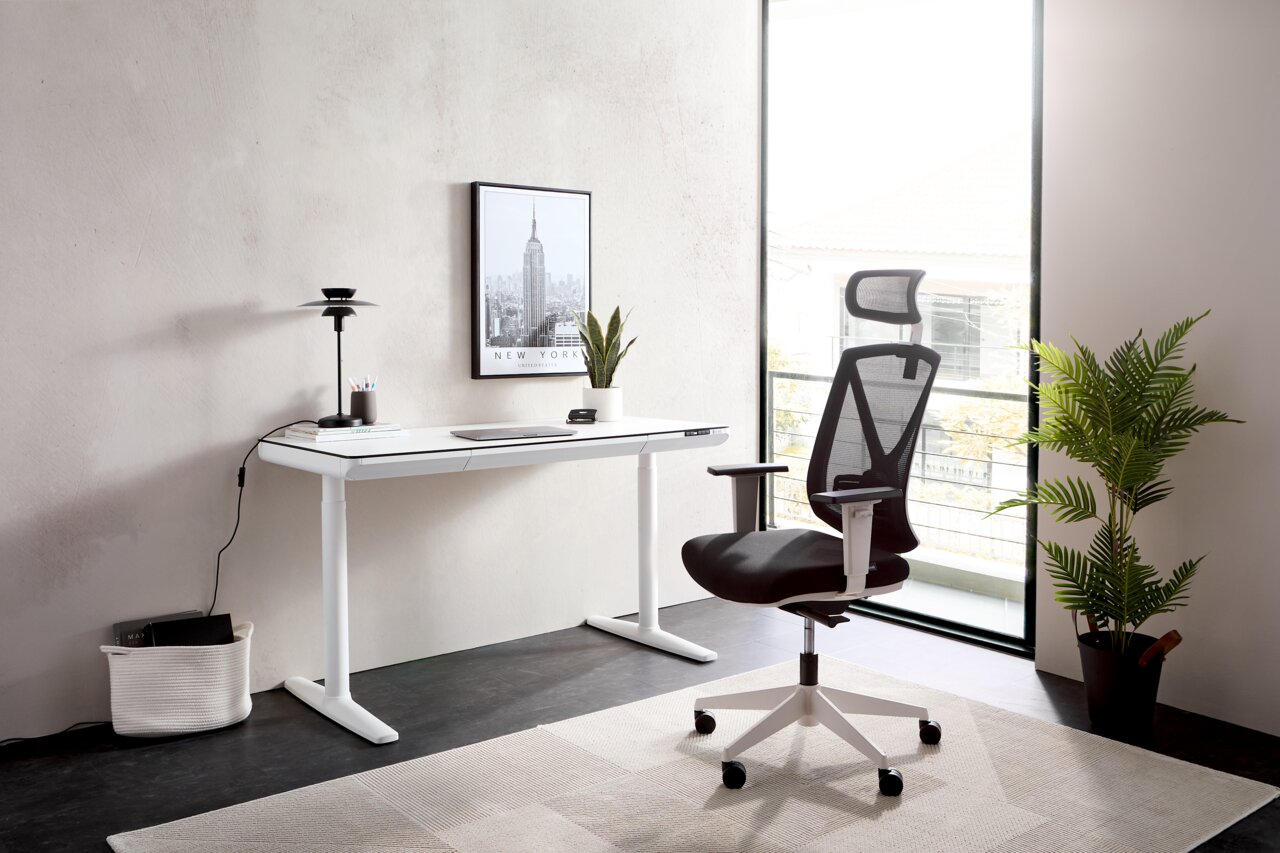 Novel E-bureau THEA 2 Modern elektrisch bureau in een lichte ruimte, gezien vanuit de zijkant, met ergonomische bureaustoel en decoratie.